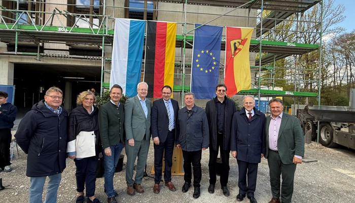 9 Personen im Halbkreis vor einem Bürogebäude (im Bau, mit Gerüst)